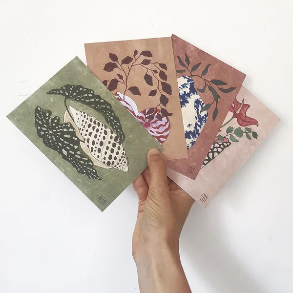 mano sosteniendo postales que muestran flores y plantas en jarrones cerámica - ilustración inspiración japonesa